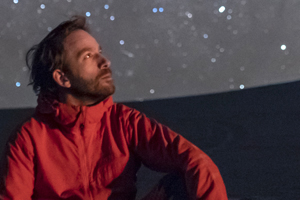 a man in a red windbreaker coat sitting looking into the night sky at the stars