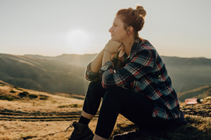 woman sitting on the ground next to a trail in the grassy foothills