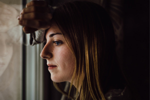 young woman with head on arm leaning against a window in a dark room
