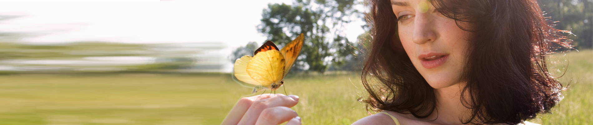 woman in a grass field looking at her hand which a butterfly has landed