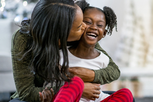 A mother kissing daughter on the cheek with a fireplace in the background