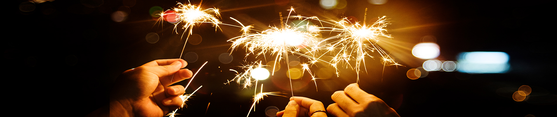 Three hands holding lit sparklers in the nigh time