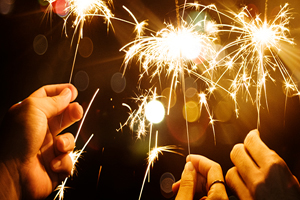 Three hands holding lit sparklers in the nigh time