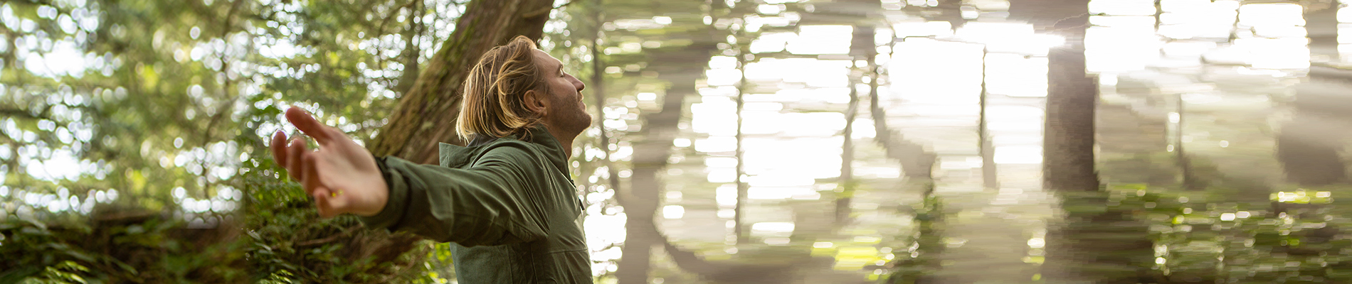 A man with open arms standing within a forest