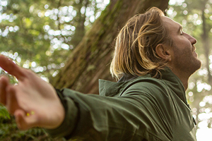 A man with open arms standing within a forest