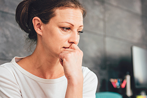 Woman standing with closed hand to mouth in thought