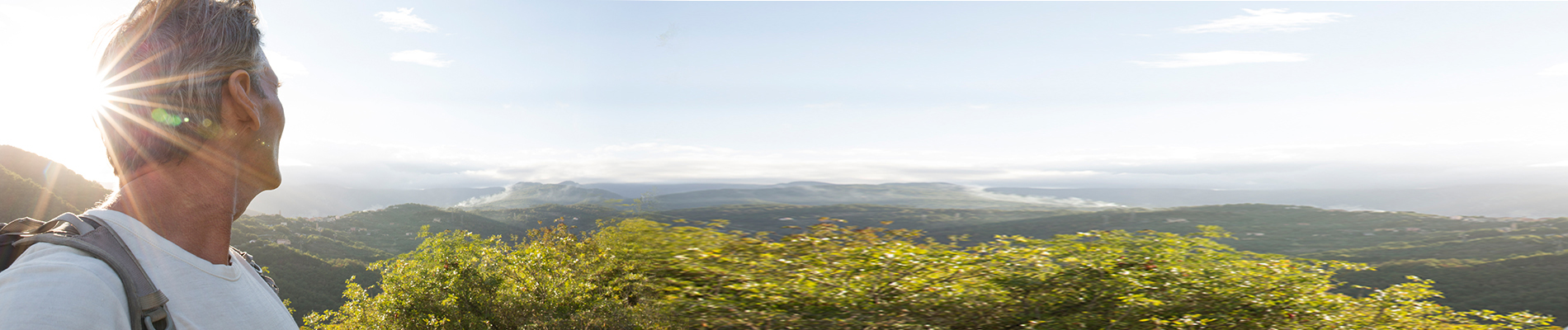 Man with a backpack looking out over a green valley