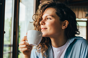 Young woman holding a cup of coffee looking out a window