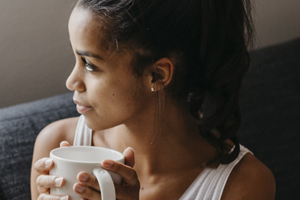 Woman gazing out window on couch with a cup of coffee