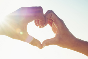 Two hands making a heart symbol towards the sky