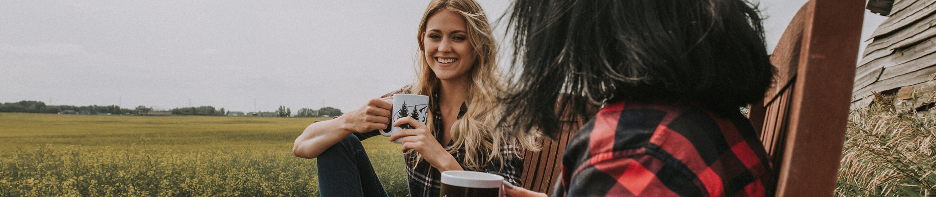 Two women having coffee sitting in chairs next to a field