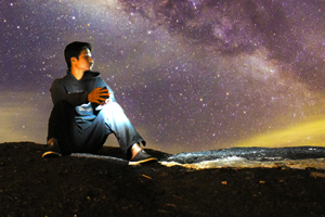 Young man sitting on the ground under the night sky