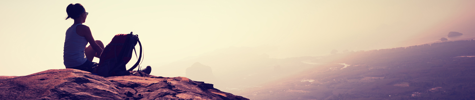 a woman sitting on a rocky bluff looking of into the distance