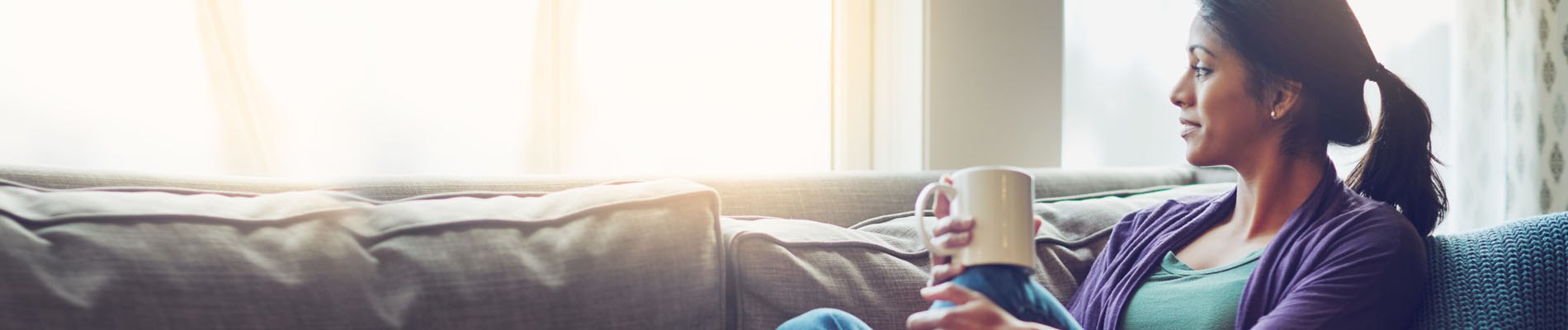 A woman sitting on a couch with a cup of coffee looking out the window