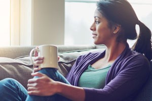 A woman sitting on a couch with a cup of coffee looking out the window
