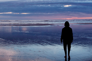 woman at day break walking across wet sand towards the ocean waves at low tide