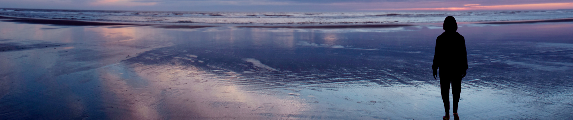 woman at day break walking across wet sand towards the ocean waves at low tide
