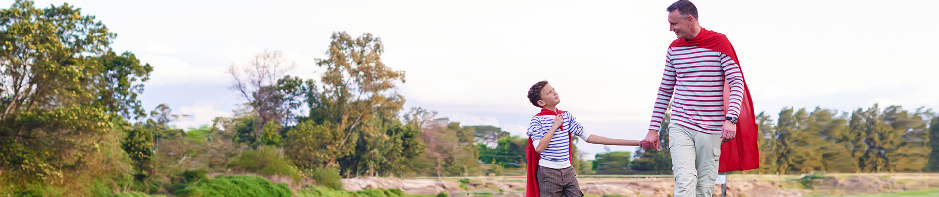 father and son in matching outfits with red capes holding hand walking on a path