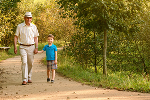 grandpa holding grandsons hand walking on a wooded park path