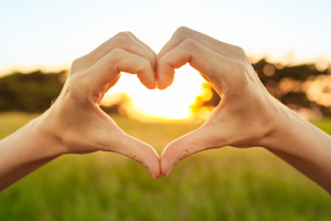Hands creating a heart with sun and field in background
