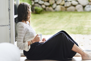 a woman sitting on the floor in an open porch doorway having coffee