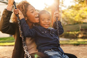 mother and son sitting in a swing at the park smiling