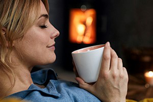 A woman sitting having coffee with eyes closed with a grin