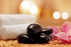 white towels, black stones, flowers and candles on a rope woven table top