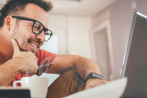 Man with glasses browsing on his laptop with his hand on his chin