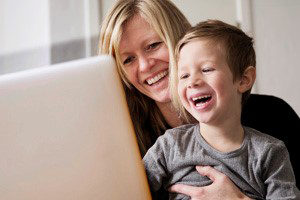 A joyful mother and child sharing smiles while gazing at a laptop