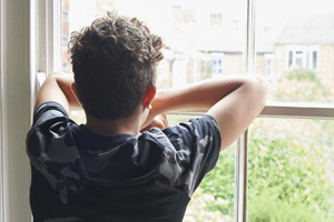 A young man gazing out the window, resting his elbows on the glass