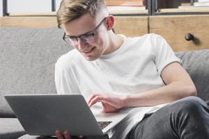 A young man lounging on a sofa, immersed in his laptop