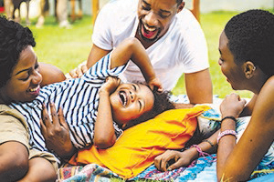 A family of four smiling while laying on a blanket in a park