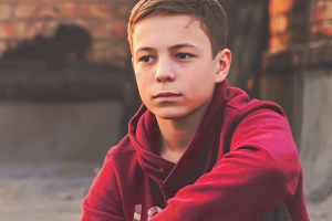 A young boy sitting with his elbow on his knee looking pensive