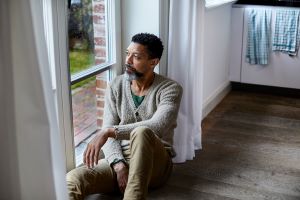 Middle aged man sitting on floor by window, looking pensive